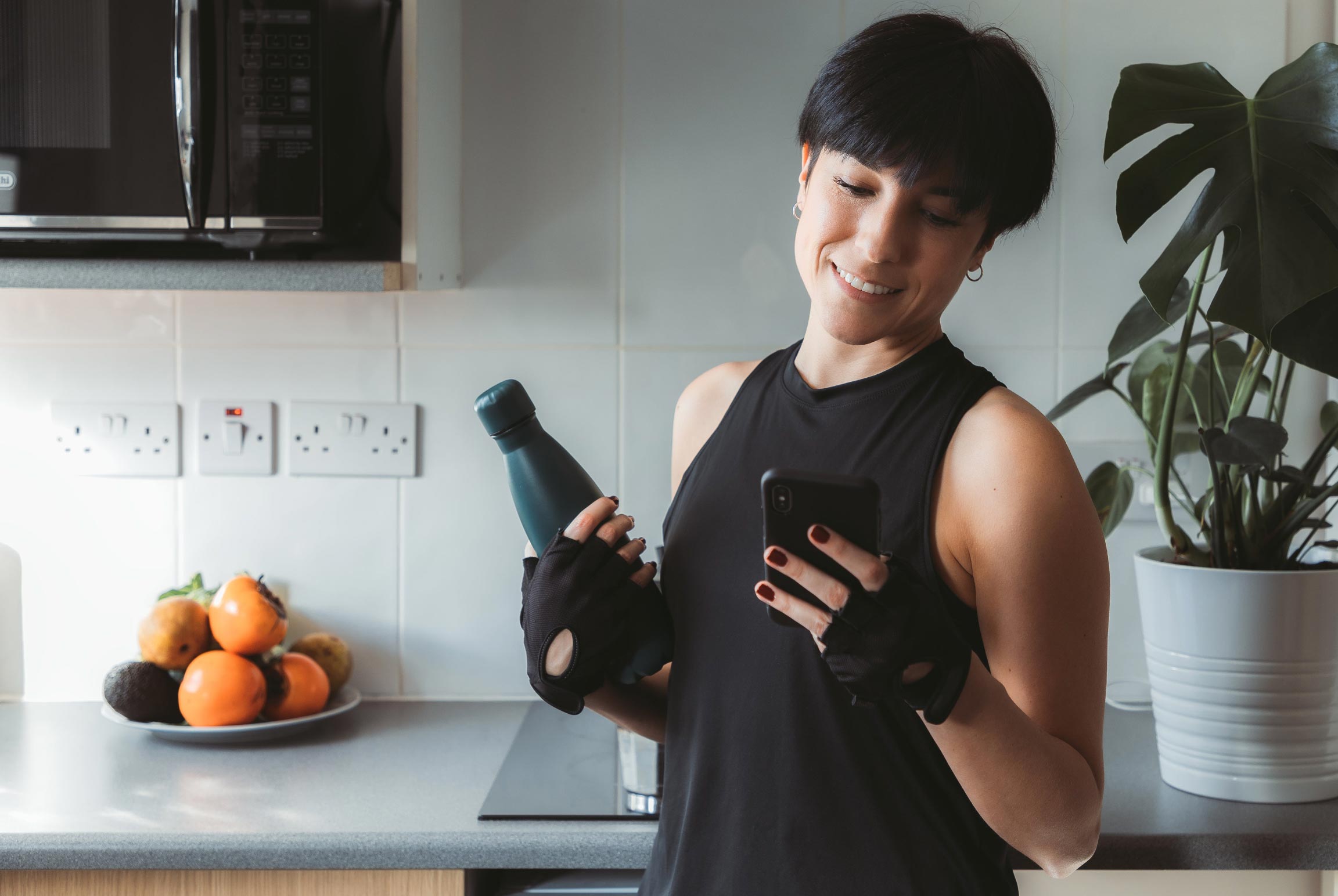 Woman holding Luxe House stainless steel water bottle in a modern home kitchen setting after a workout